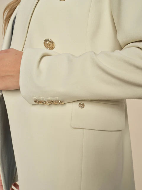 close up tp the Babeth Luni Blazer in cream. This blazer pays tribute to the timeless style of MOS MOSH. Crafted in a double-breasted design, it boasts an elongated and oversized silhouette, adorned with exquisite gold-embossed buttons. 